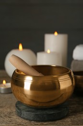 Golden singing bowl, mallet and burning candles on wooden table, space for text