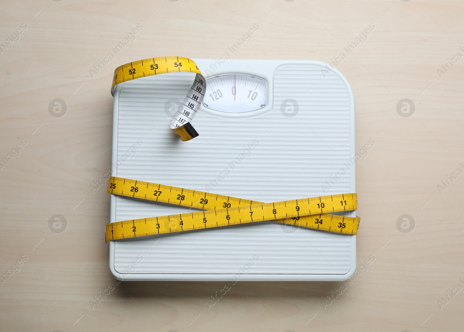 Photo of White bathroom scale and measuring tape on wooden floor, top view. Weight loss concept