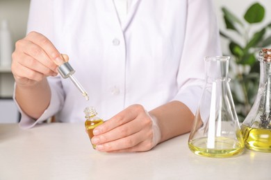 Dermatologist developing cosmetic oil at white table indoors, closeup