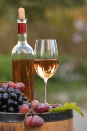 Photo of Delicious wine and ripe grapes on wooden barrel outdoors