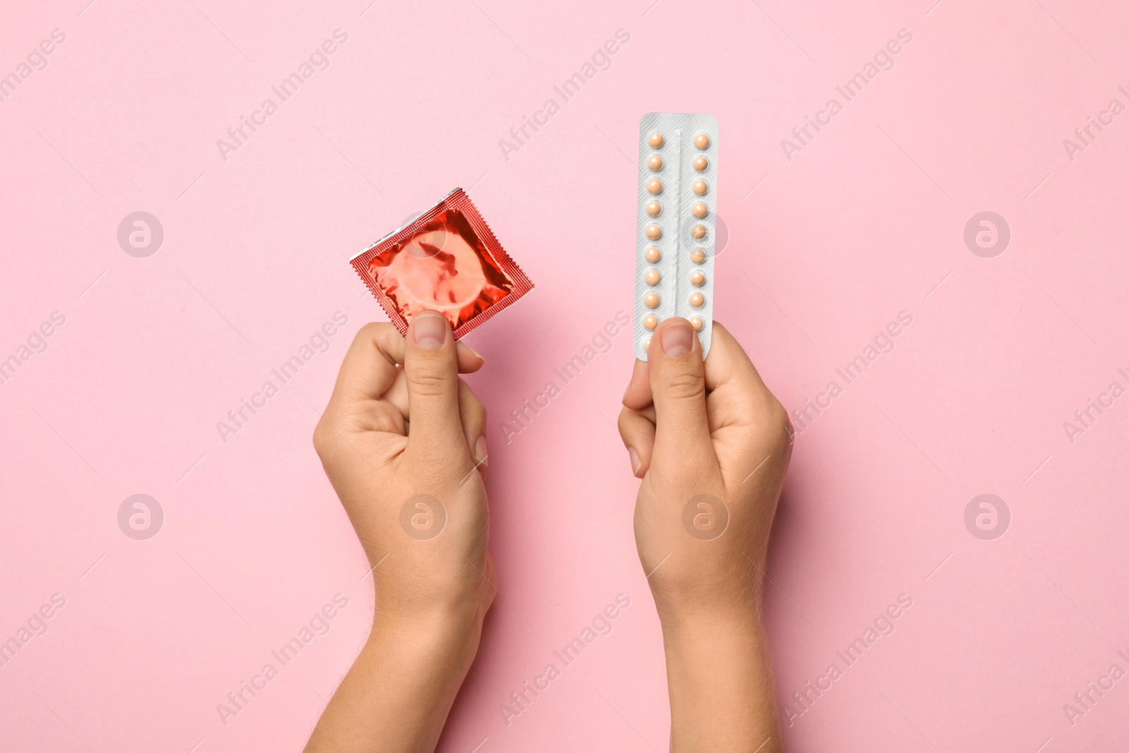 Photo of Woman holding condom and birth control pills on pink background, top view. Safe sex