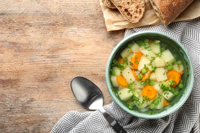 Bowl of fresh homemade vegetable soup served on wooden table, flat lay. Space for text