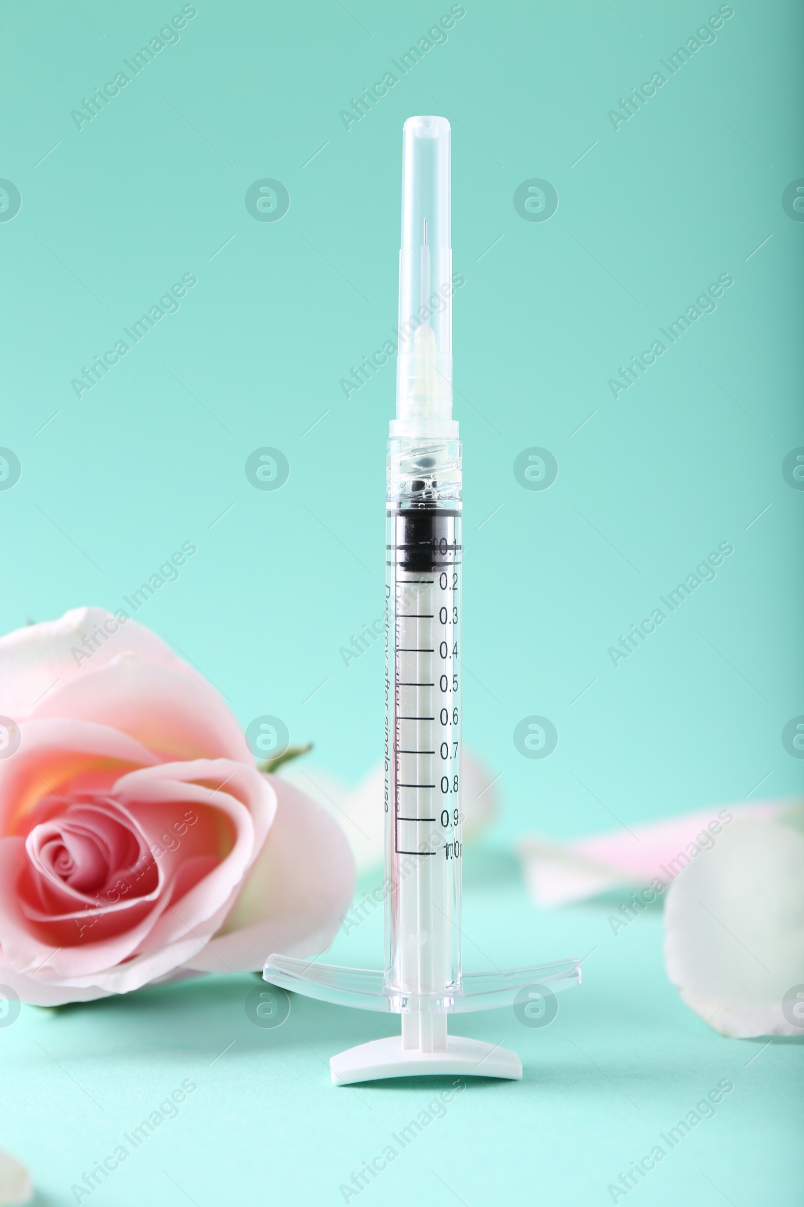 Photo of Cosmetology. Medical syringe, rose flower and petals on turquoise background