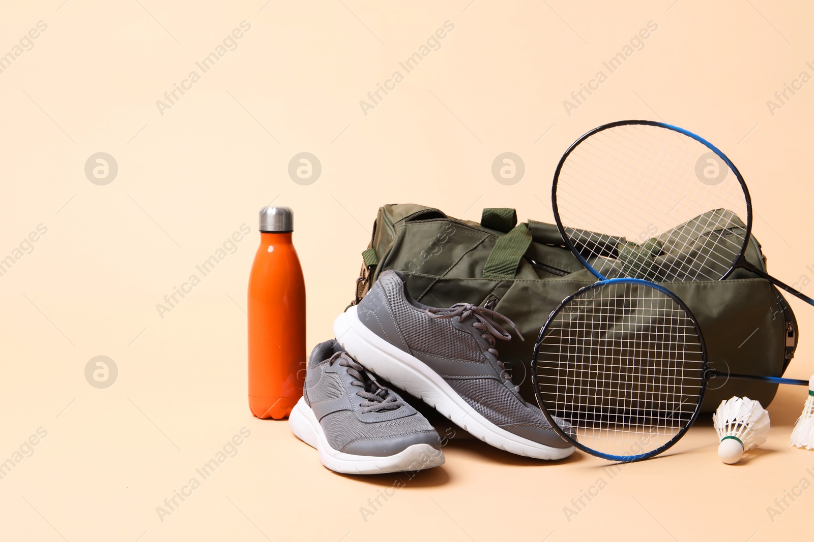 Photo of Badminton set, bag, sneakers and bottle on beige background, space for text
