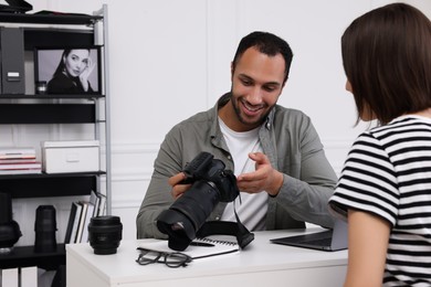 Photo of Young professional photographer showing camera to woman in modern photo studio