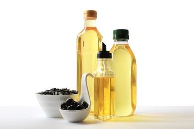 Photo of Bottles of different cooking oils, olives and sunflower seeds on white background