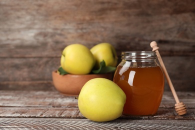 Jar of honey, apples and dipper on wooden table