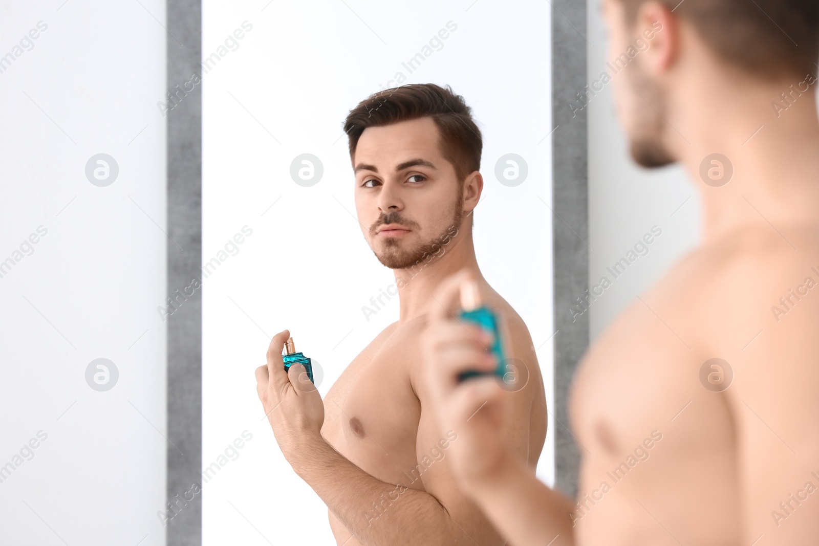 Photo of Handsome man using perfume in front of mirror