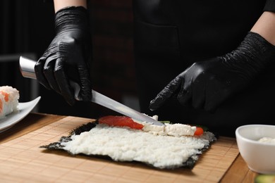 Chef in gloves making sushi roll at wooden table, closeup