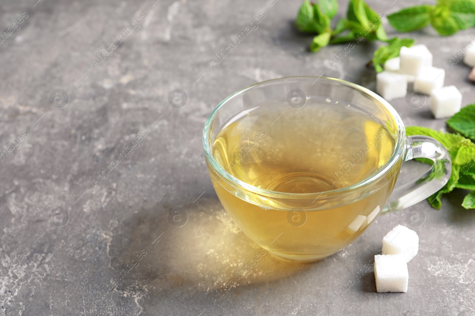 Photo of Cup with hot aromatic mint tea, fresh leaves and sugar cubes on table