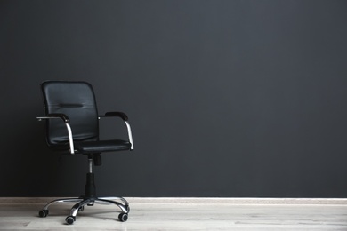 Photo of Comfortable office chair near black wall indoors. Space for text