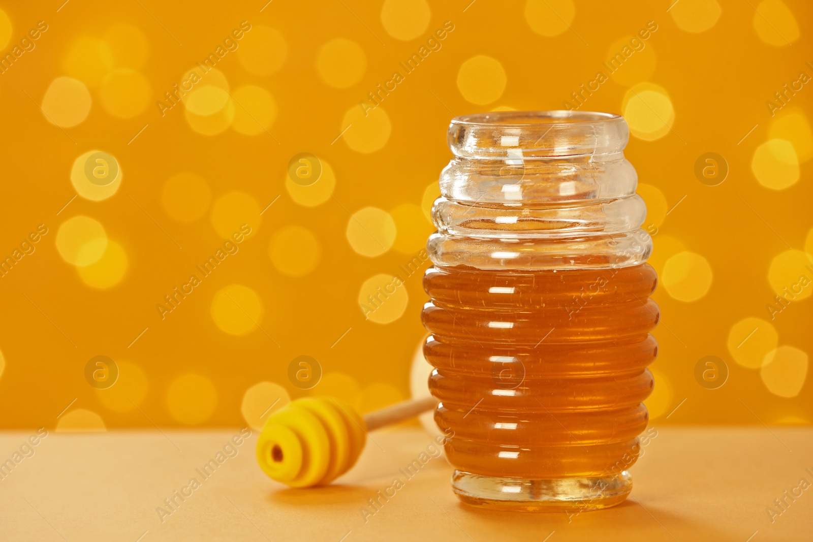 Photo of Jar with fresh honey on table against blurred background. Space for text