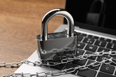 Photo of Cyber security. Laptop with padlock and chain on wooden table, closeup