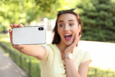 Photo of Young woman taking selfie outdoors on sunny day