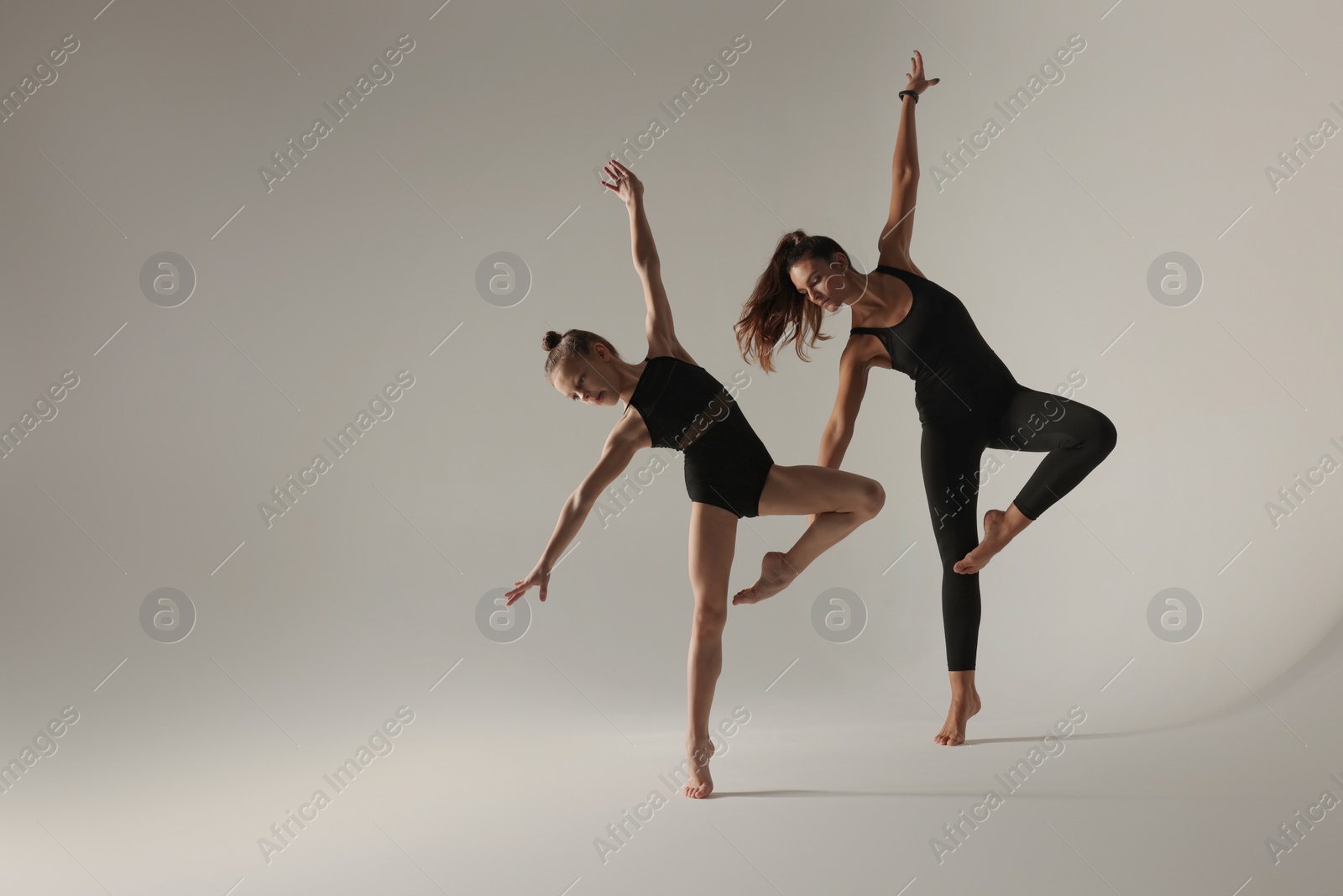 Photo of Little girl and her coach doing gymnastic exercise on white background