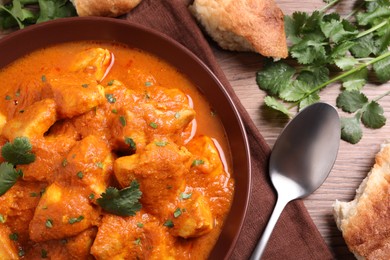 Photo of Bowl of delicious chicken curry on wooden table, flat lay