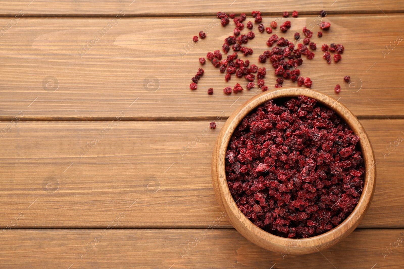 Photo of Dried red currants and bowl on wooden table, flat lay. Space for text