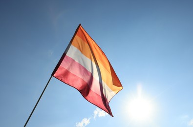 Photo of Woman holding bright lesbian flag against blue sky, space for text