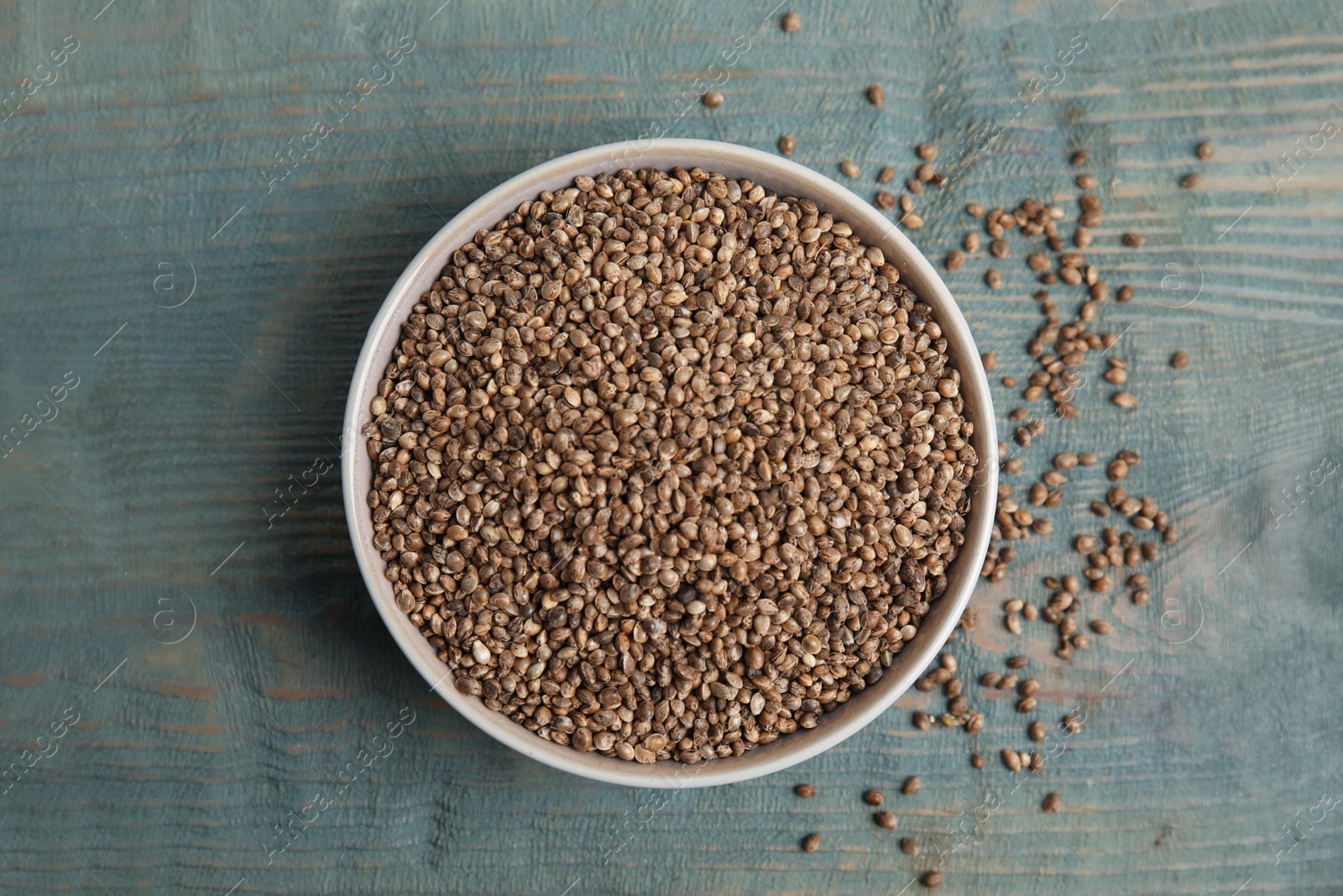 Photo of Bowl with organic hemp seeds on light blue wooden table, flat lay