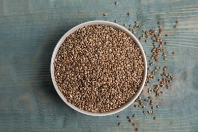 Photo of Bowl with organic hemp seeds on light blue wooden table, flat lay