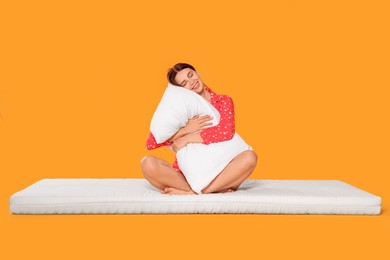 Photo of Young woman on soft mattress holding pillow against orange background