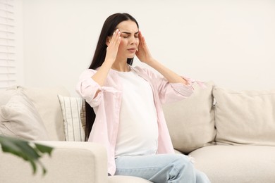 Photo of Pregnant woman suffering from headache on sofa at home