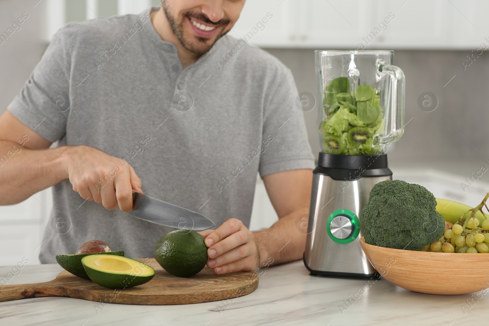 Photo of Man cutting avocado for delicious smoothie at white marble table in kitchen, closeup