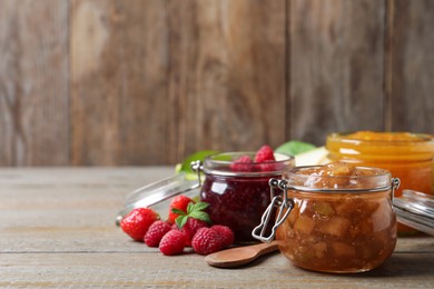 Photo of Jars with different jams and fresh berries on wooden table. Space for text