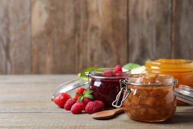 Jars with different jams and fresh berries on wooden table. Space for text