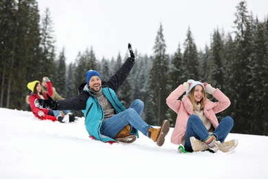 Happy friends sliding on sleds outdoors. Winter vacation