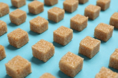 Photo of Brown sugar cubes on turquoise background, closeup
