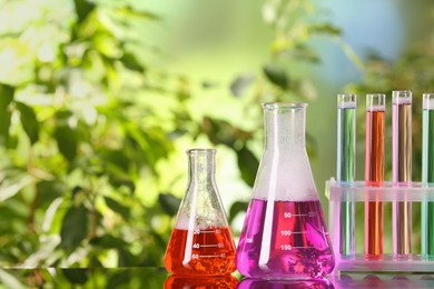 Photo of Laboratory glassware and test tubes with colorful liquids on glass table outdoors, space for text. Chemical reaction