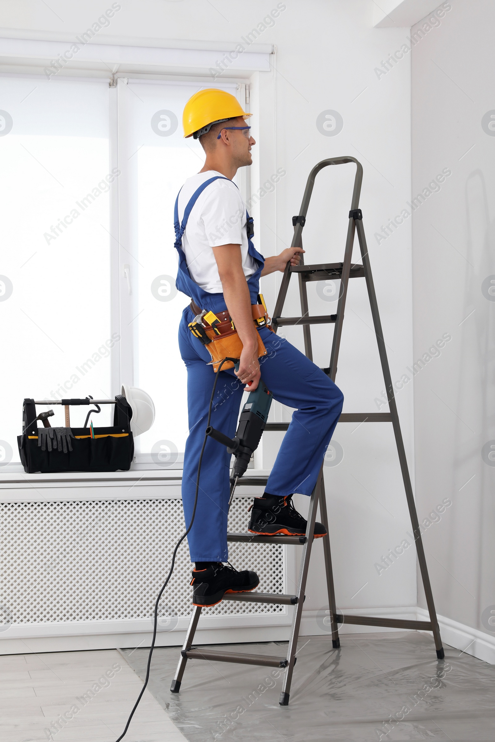 Photo of Worker with electric drill on ladder indoors