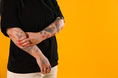 Photo of Young woman with tattoos on arms against yellow background, closeup. Space for text