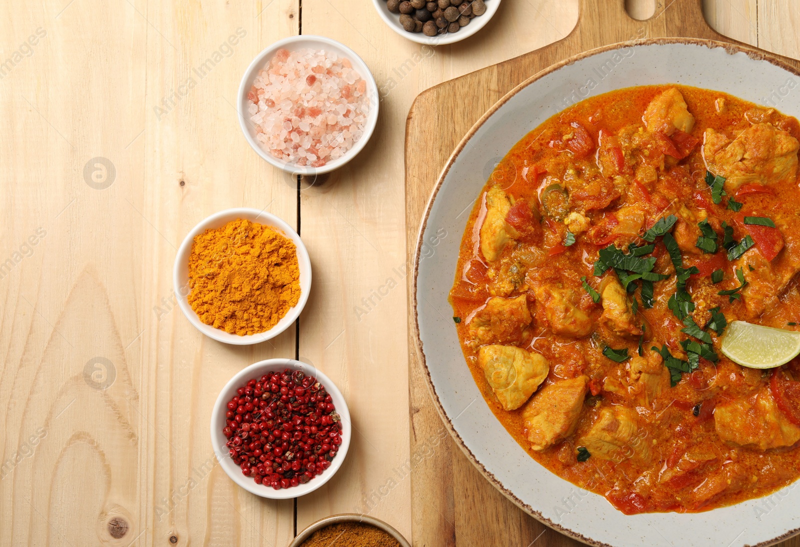 Photo of Delicious chicken curry and spices on wooden table, flat lay. Space for text