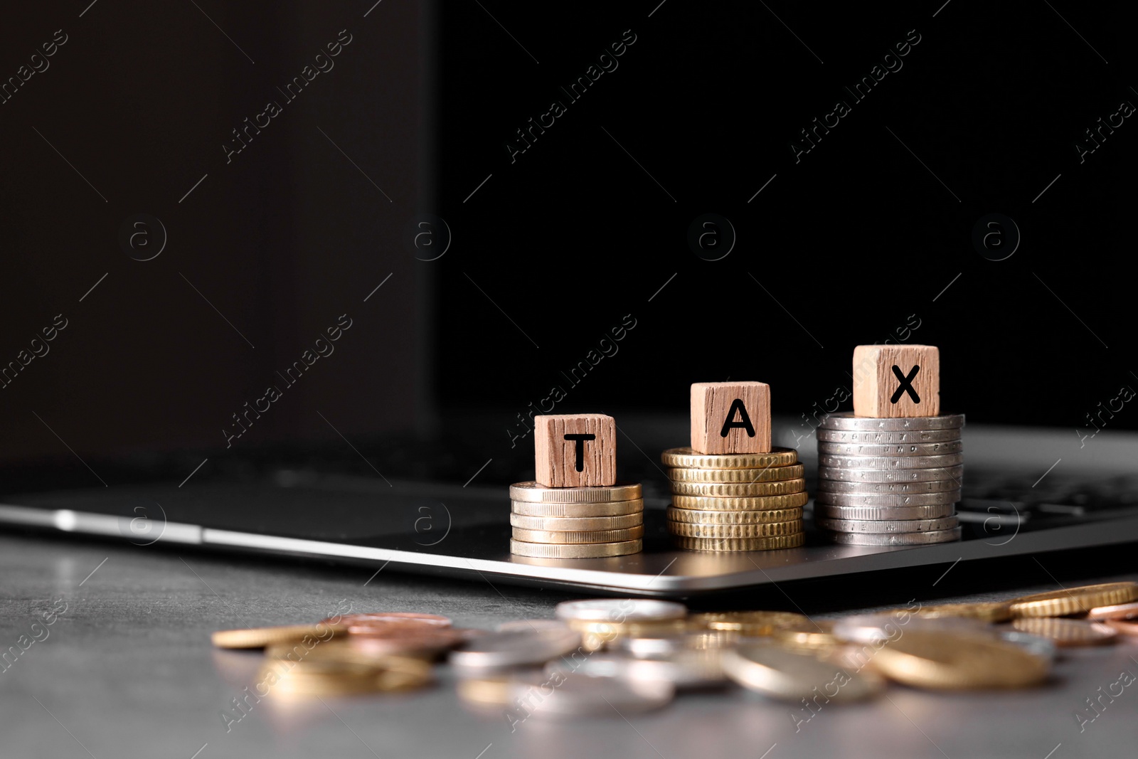 Photo of Word Tax made of wooden cubes, laptop and coins at grey table, space for text