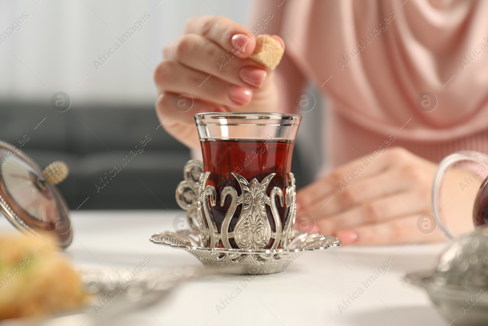 Photo of Woman adding sugar to delicious Turkish tea at white table, closeup