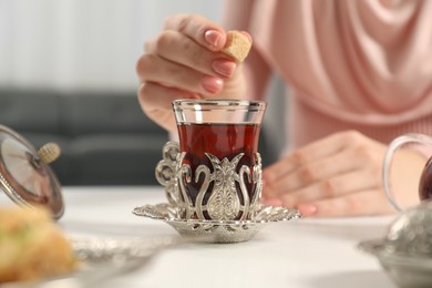 Photo of Woman adding sugar to delicious Turkish tea at white table, closeup