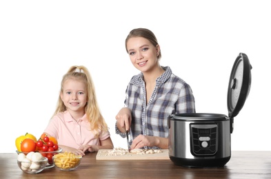 Mother and daughter preparing food with modern multi cooker at table against white background