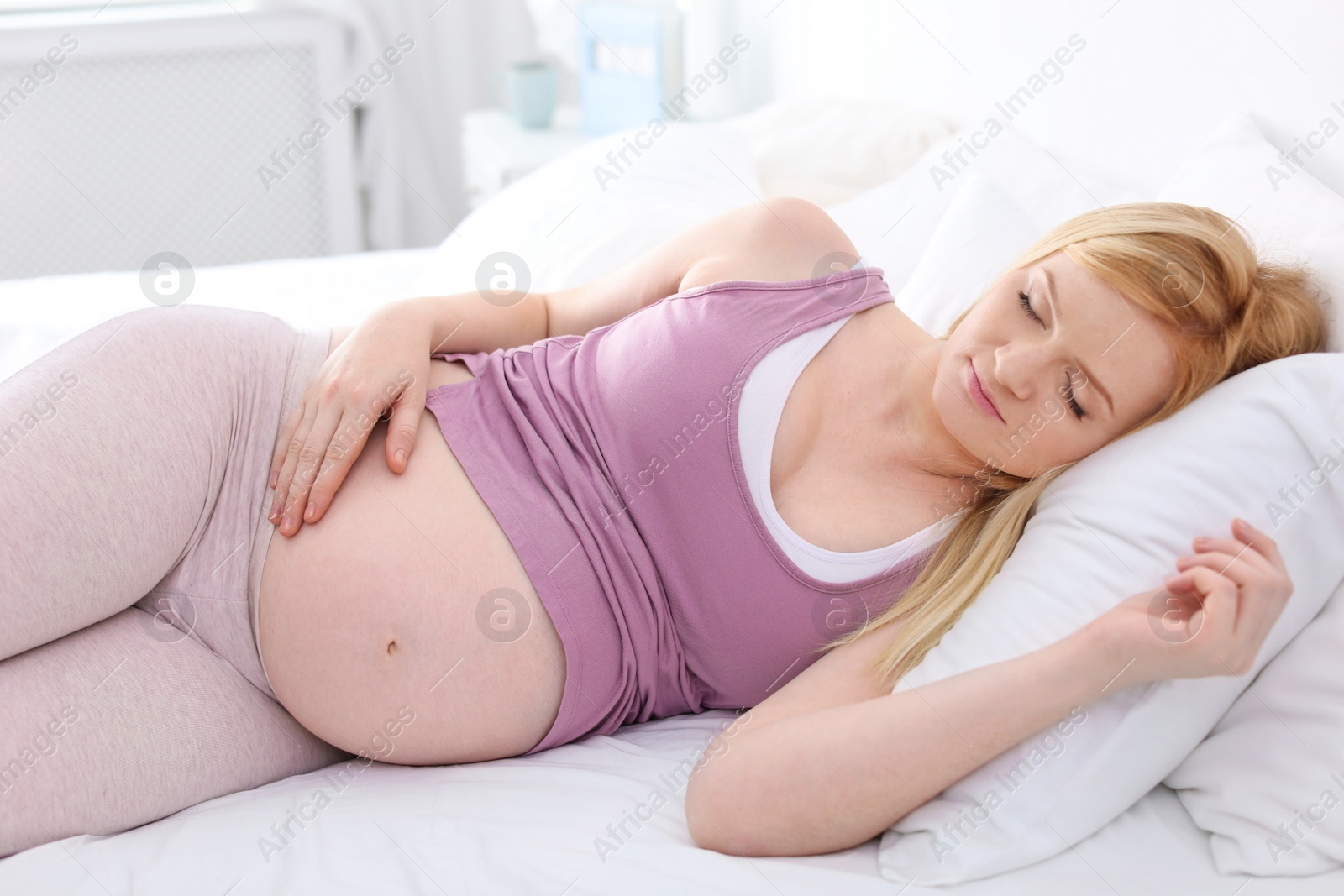 Photo of Young pregnant woman sleeping on bed in light room