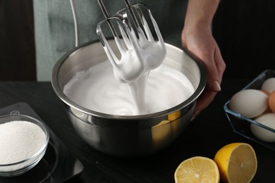 Photo of Woman making whipped cream with hand mixer at black table, closeup