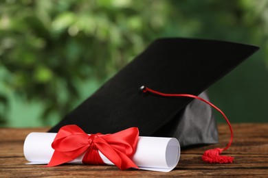 Photo of Graduation hat and diploma on wooden table against blurred background
