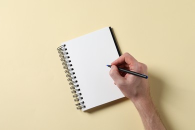 Man with pen and empty notepad on yellow background, top view