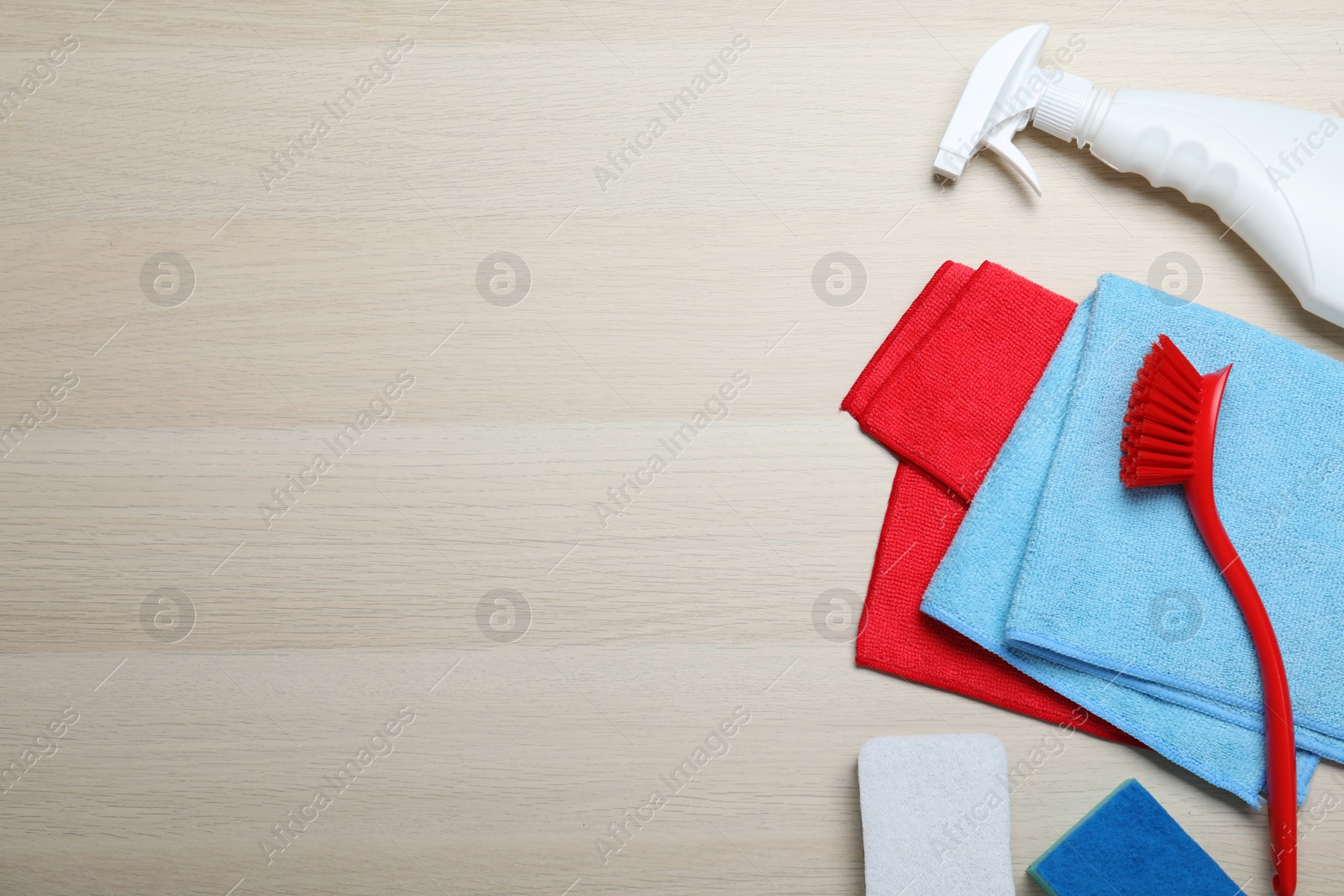 Photo of Microfiber cloths and cleaning supplies on light wooden background, flat lay. Space for text