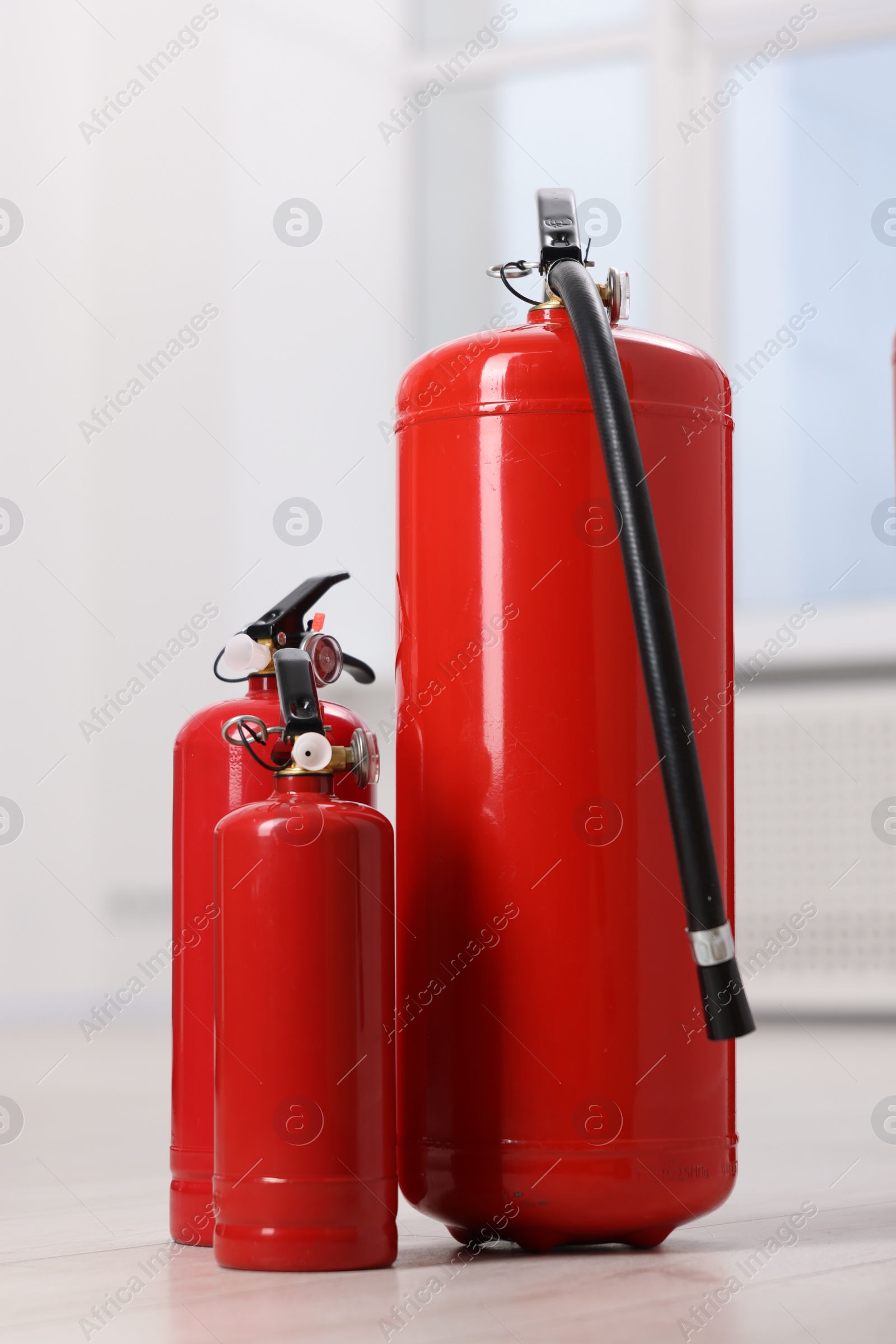 Photo of Three fire extinguishers on floor indoors, closeup