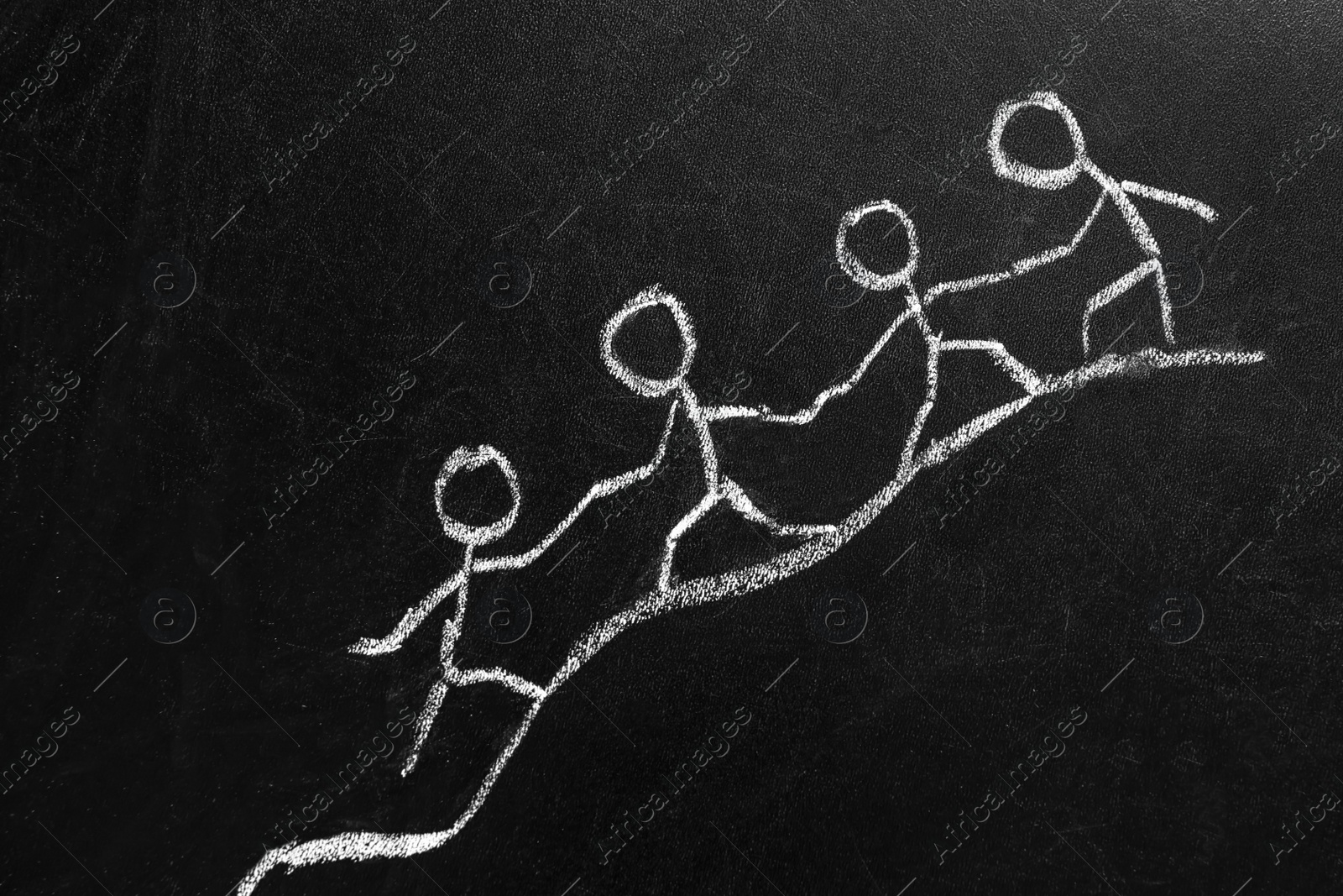 Photo of Drawing of people holding hands and climbing together on chalkboard. Unity concept