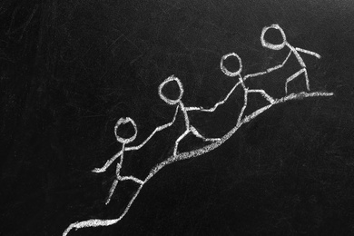 Photo of Drawing of people holding hands and climbing together on chalkboard. Unity concept