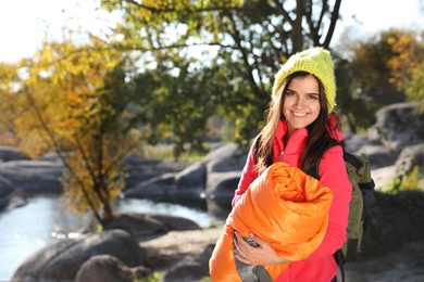 Female camper with sleeping bag near beautiful lake. Space for text