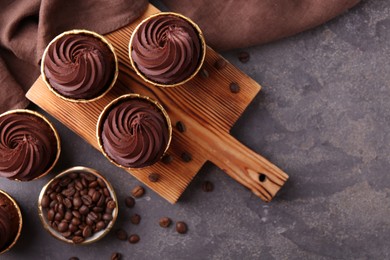Photo of Delicious chocolate cupcakes and coffee beans on grey textured table, flat lay