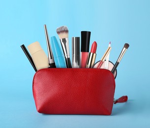 Image of Cosmetic bag filled with makeup products on light blue background